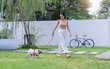 Asian young woman in casual walk with her pug dog on a red leash, enjoying a relaxed walk beside a stationary bicycle. Home relax recreation activities, happy minimal lifestyle.