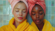 Two multiethnic women dressed in yellow bathrobes after beauty treatments, close-up portrait.