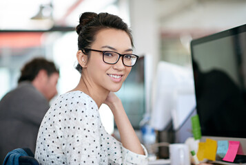 Portrait, smile and creative business woman in office at startup company on computer in Greece. Face, professional entrepreneur and happy employee, worker or web developer in glasses at workplace