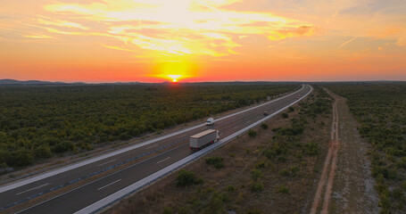 Wall Mural - AERIAL: Orange sunrise sunbeams illuminate truck driving across rural Croatia.