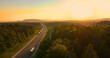 AERIAL, LENS FLARE: Beautiful morning above lush forest surrounding the highway. Smooth running traffic with fast driving cars and trucks on a motorway leading through picturesque hilly countryside.