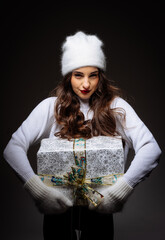 Wall Mural - A woman is holding a white box with a red ribbon on it. She is wearing a white sweater and a white hat.