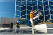 © Kitreel - Vibrant Outdoor Scene Captures A Young Woman In A Yellow Top And Purple Hat Dancing Energetically, With A Male Spectator In Yellow Pants And A Blue Hat, Against A Modern Glass Building Background.