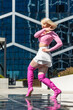 Stylish Woman In Pink Top And White Skirt Paired With Pink Thigh-High Boots Strikes A Pose Against A Modern Glass Building Background. Vertical Screen. Perfect For Fashion And Lifestyle Content.