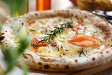 Fototapeta Tulipany - Wood fired pizza with cheese, smoked salmon, onion, rosemary, on a wooden cutting board, selective focus, close up.