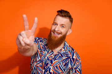 Photo of cool positive guy dressed print shirt showing you v-sign isolated orange color background