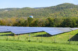 Fenced solar power plant with forested mountains in background on a clear autumn day