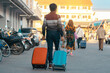 Back view of elderly traveler man in casual clothes dragging suitcase . Senior man walking with his luggage on street in morning. Male tourist with luggage for vacation. Vacation and travel concept.