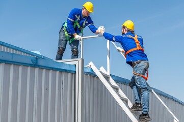 Two construction workers wearing safety gear climb up a ladder to the roof of a building