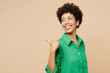 © ViDi Studio - Young happy fun woman of African American ethnicity wear green shirt casual clothes point thumb finger aside indicate on area isolated on plain pastel light beige background studio. Lifestyle concept.