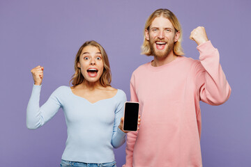 Wall Mural - Young couple two friends family man woman wear pink blue casual clothes together hold in hand use mobile cell phone with blank screen area do winner gesture isolated on pastel plain purple background.