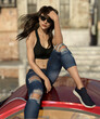 Illustration of a beautiful young woman with dark hair wearing sunglasses sitting on a car with buildings in the background.