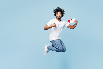 Wall Mural - Full body young happy Indian man wear white t-shirt casual clothes jump high hold gift certificate coupon voucher card for store isolated on plain pastel light blue cyan background. Lifestyle concept.