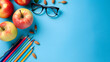 A colorful composition of stationery, apples and glasses on blue background with copy space. Teachers day. Back to school. Student day