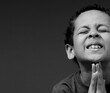 boy praying to God with hands together on grey black background with people stock image stock photo	