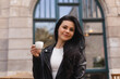 © zvkate - Portrait of joyful young woman enjoying a cup of tea and aroma at restaurant. Smiling pretty girl drinking hot tea or coffee in cafe. Excited woman wearing black jacket, white t-shirt and laugh.