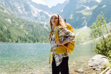 Happy tourist woman  enjoys the view of the mountain lake in sunny weather. Scenery of the majestic mountains. Active lifestyle.