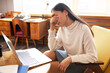 Indoor side view portrait of young elegant woman sitting in front of laptop at working table doing facepalm gesture after making mistake working in her office. Online tutor failed to explain new topic