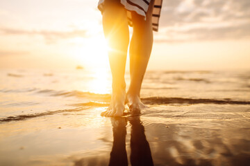 Slim female legs and feet walking along sea water waves on sandy beach. Pretty woman walks at seaside surf. The concept of relax, travel, freedom and summer vacation.