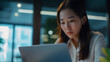 © Natali - Asian businesswoman using laptop while analyzing reports in office.