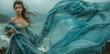 woman in a long flowy aquamarine colour dress standing outside in the wind with sea and mountain in the background. 