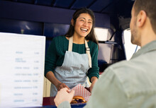 A Friendly Food Truck Worker Shares A Laugh With A Customer During A Sunny Day's Service