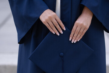 Young female hands holding navy graduation cap, horizontal
