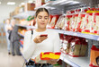 Girl buyer examines packaging of product and scan QR code on label. Young woman in supermarket view and buys daily groceries, pasta Chinese noodles