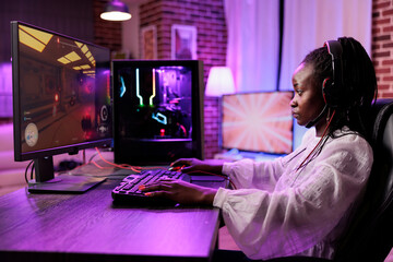 Wall Mural - Woman in brick wall living room playing SF video game on gaming PC at computer desk late at night. Tired gamer girl battling hostiles in online multiplayer futuristic shooter