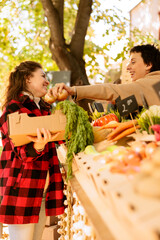 Wall Mural - Happy female client buying organic bio fruits and vegetables at local farmers market. Cheerful customer holding box with various seasonal produce at harvest fair festival booth.