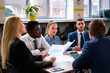 © artiemedvedev - Multiethnic group of professionals engaged in a business meeting. African, Asian, and Caucasian team members discuss charts, collaborate on project in modern office setting.