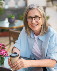 A woman is sitting at a table with a cup of coffee in front of her. She is smiling and she is enjoying her time