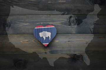 wooden heart with national flag of wyoming state near united states of america map on the wooden background.