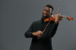 African American man in a black suit playing the violin on a gray background in a captivating musical performance portrait