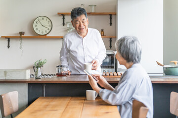 Poster - キッチンでコーヒーを淹れる高齢者男性とダイニングテーブルでスマホを使う高齢者女性
