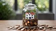 A glass jar filled with pennies has a small house sitting on top of the coins. The jar is sitting on a wooden table with other pennies scattered on the table. There is a blurred background with a plan