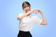 Portrait Asian student girl with Thai university uniform making heart signal isolated on blue background.