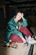 © AnnaStills - Vertical flash shot of young Caucasian woman in streetwear sitting on floor in skatepark listening to music on retro portable player