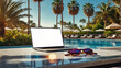 Laptop with a blank white screen mock up on table in tropical hotel with palm trees on swimming pool on trip. Remote work on vacation and travel, home office, internet, tours, resort