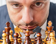 Business man executive pondering on chessboard in close-up on wooden chess pieces in game concept
