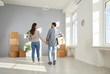 Young couple moving into their new home. Back view of happy, loving man an woman holding hands and standing together in spacious empty unfurnished living room in their new house or apartment
