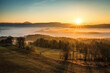 The sun illuminates a valley with thick inversion fog, wind farms and the Královecký špičák mountain in the background on a cold morning in early autumn near Trutnov