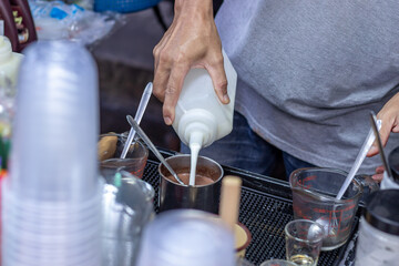 Wall Mural - Male merchant is pouring milk into a bottle with coffee to mix it in an iced milk coffee menu, Cold milk coffee is a popular drink in Thailand