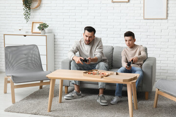 Canvas Print - Father and his little son with pizza playing video games on sofa at home