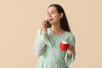 Poster - Happy young woman holding cup with marshmallows on beige background