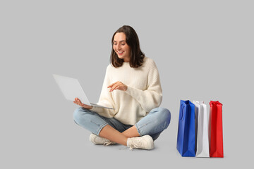 Poster - Young woman with laptop and shopping bags on white background