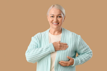 Wall Mural - Mature woman checking her breast on brown background. Cancer awareness concept