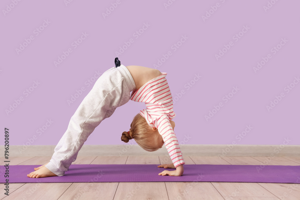 Cute little girl practicing yoga on mat against lilac background