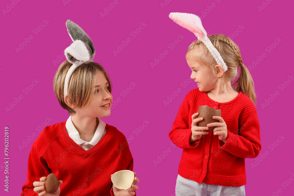 Cute little children in bunny ears with chocolate eggs on purple background. Easter celebration