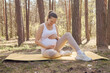 Pregnancy meditating recreation. Caucasian pregnant woman doing yoga on mat relaxing care tummy enjoying sport exercises in open air stroking belly resting after forest workout